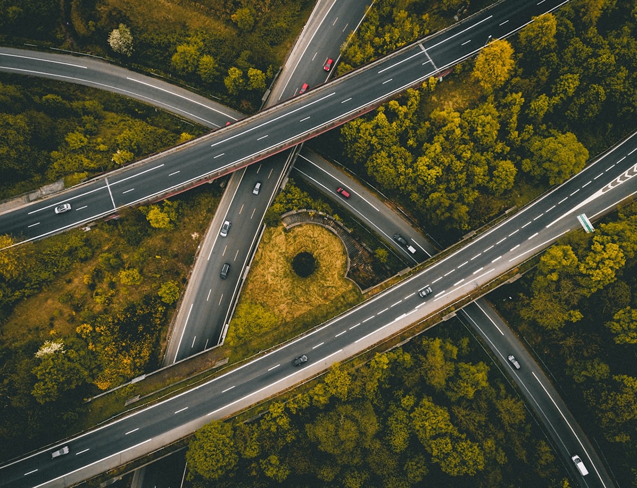 Flygbild av motorvägskorsning omgiven av träd, med bilar som kör i olika riktningar.