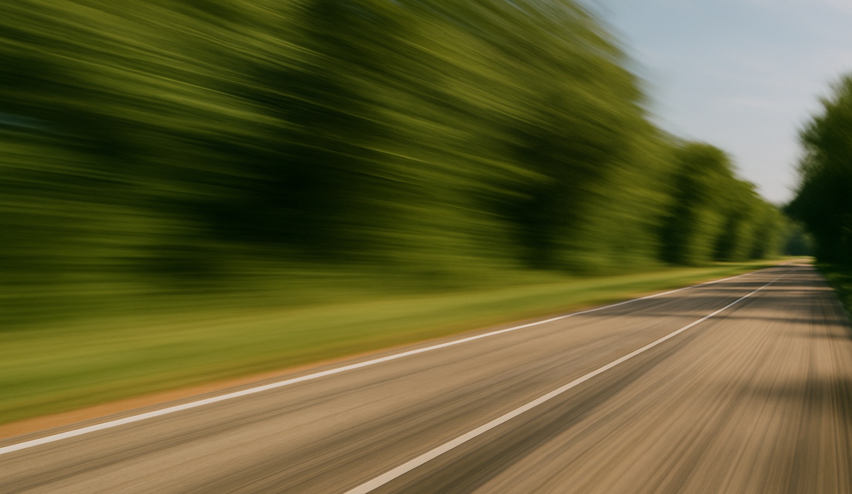 Suddig bild av en väg kantad av träd som ger en känsla av hastighet.