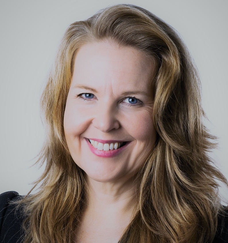 Kvinna med långt ljusbrunt hår och blå ögon ler mot kameran.