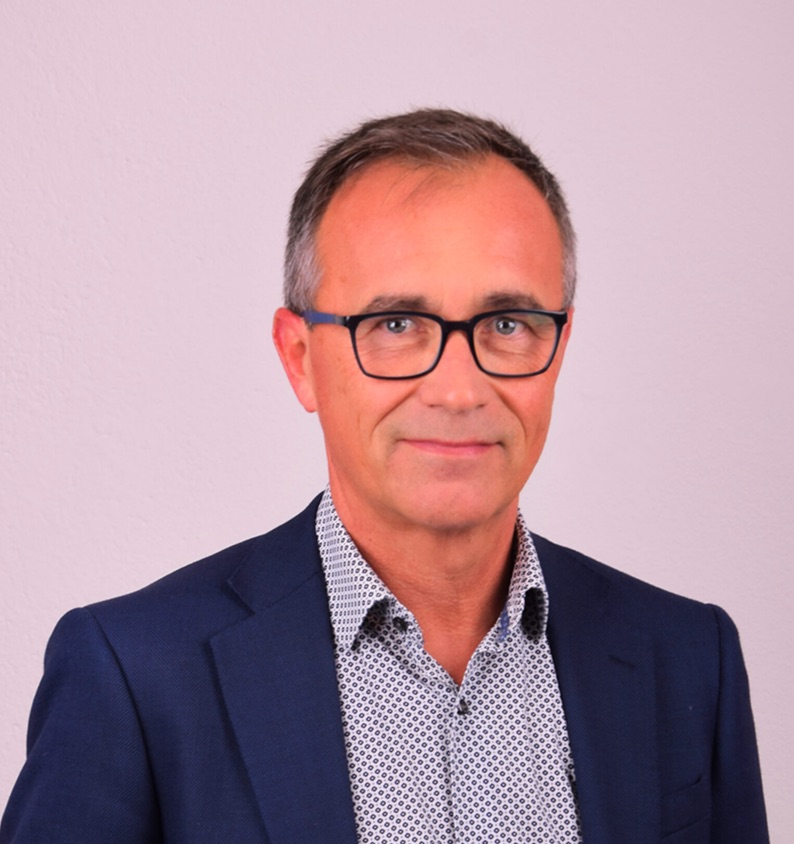 En man i blå kavaj och glasögon står mot en vit bakgrund.