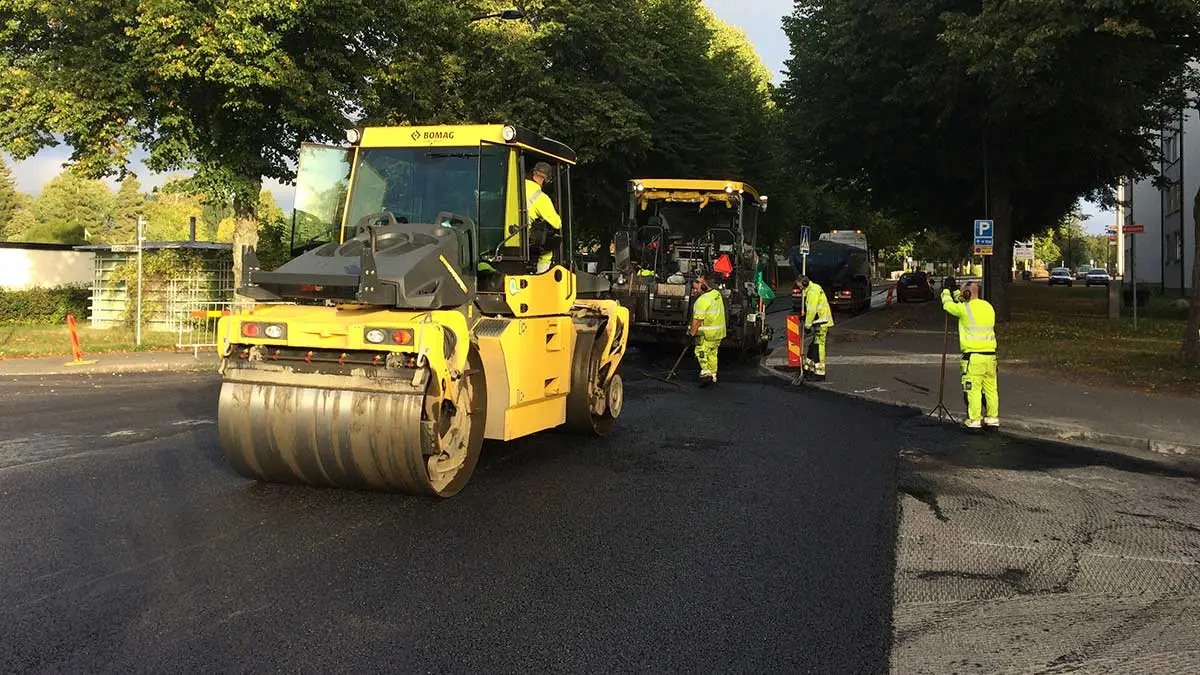Vält och arbetare lägger ny asfalt på gata.